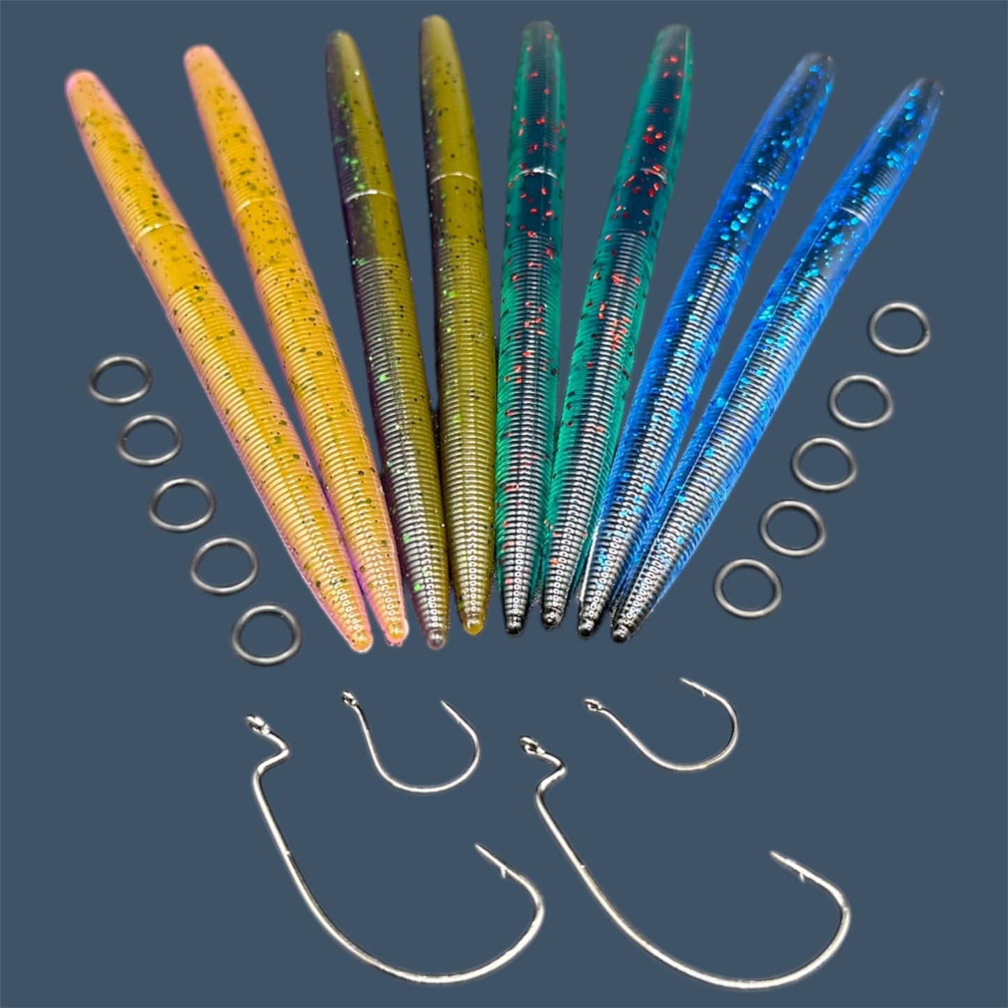 Big League Bait Company Boombox this kit is pictured with several bags of soft plastic fishing lures. All of the soft plastic baits are Big League Bait Company's Boomstick. A senko style stick bait with Wacky Rig O-rings, Eagle Claw EWG 4/0 Hooks and Wacky Rig hooks. Shown in 4 colors (left to right) Chameleon, Swamp Juice, Dark Emerald (Core Shot Stick Back), and Black N Blue (Core Shot Stick Bait)